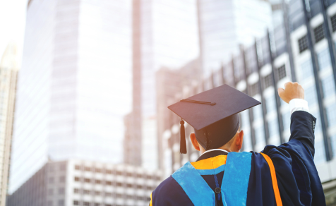 Higher Ed graduate celebrating with cap and gown in city